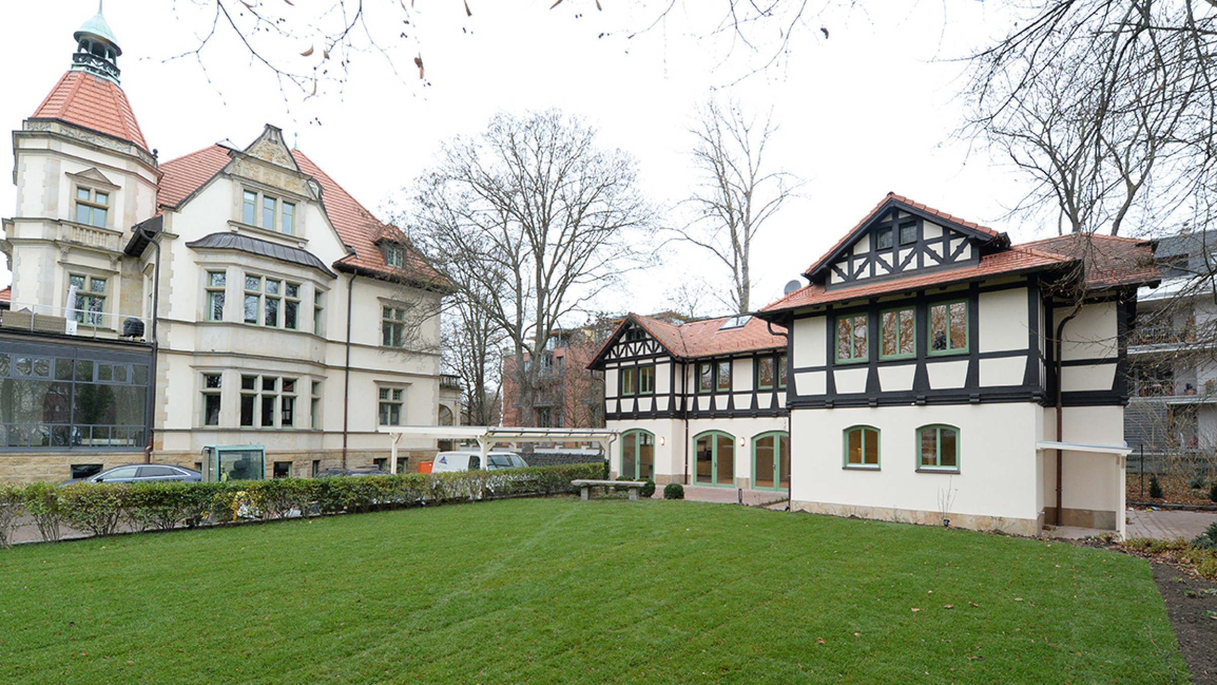 Denkmalgesch&uuml;tzte Villa mit Turm, rechts daneben das Kutscherhaus mit Fachwerkgiebel, davor eine Rasenfl&auml;che.