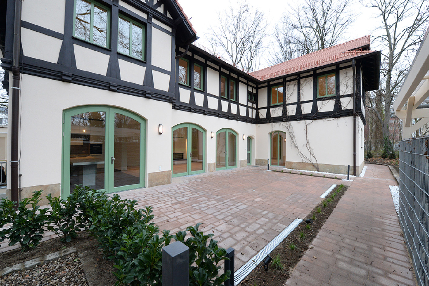 Der gepflasterte Hof entlang der Fachwerkfassade mit gr&uuml;n gefassten Bogent&uuml;ren und neu gesetzten Hecken.