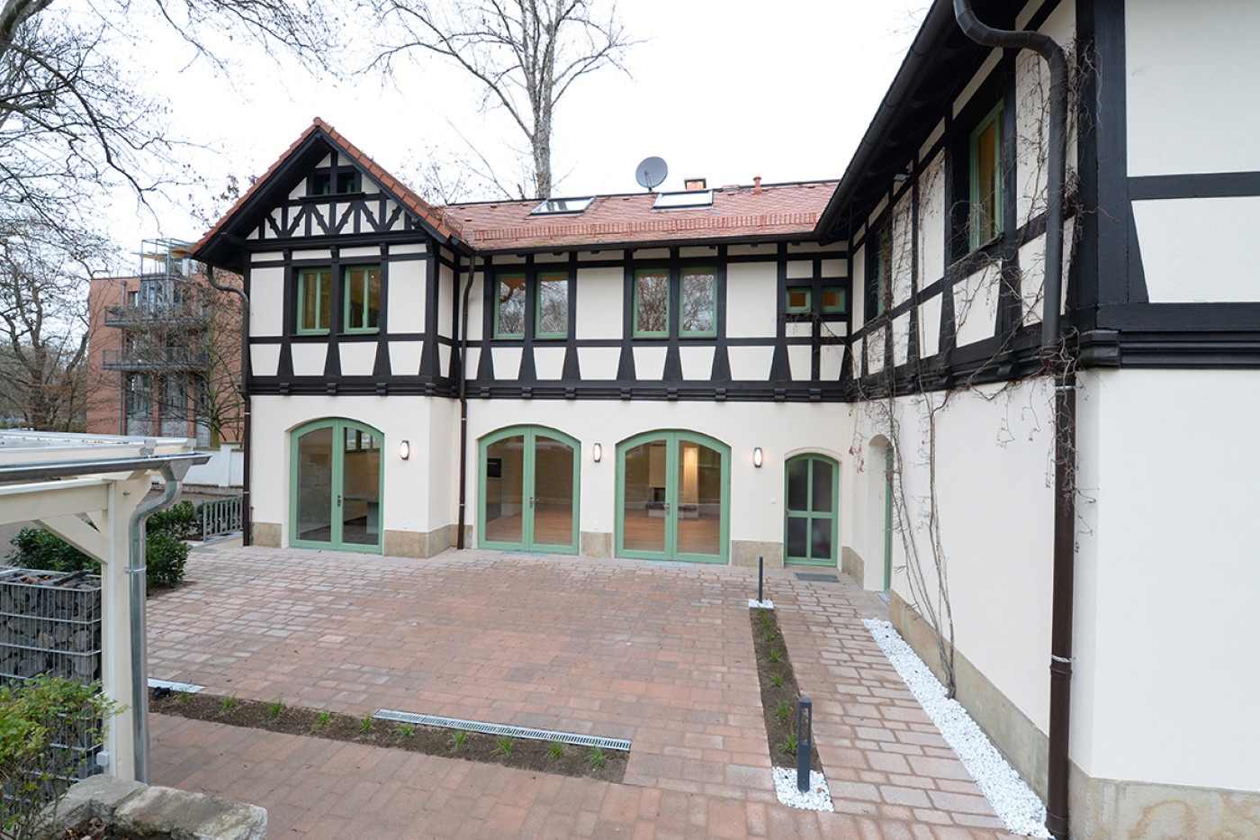 Innenhof zwischen Villa und Kutscherhaus mit gepflastertem Belag und gr&uuml;n gefassten Rundbogent&uuml;ren.