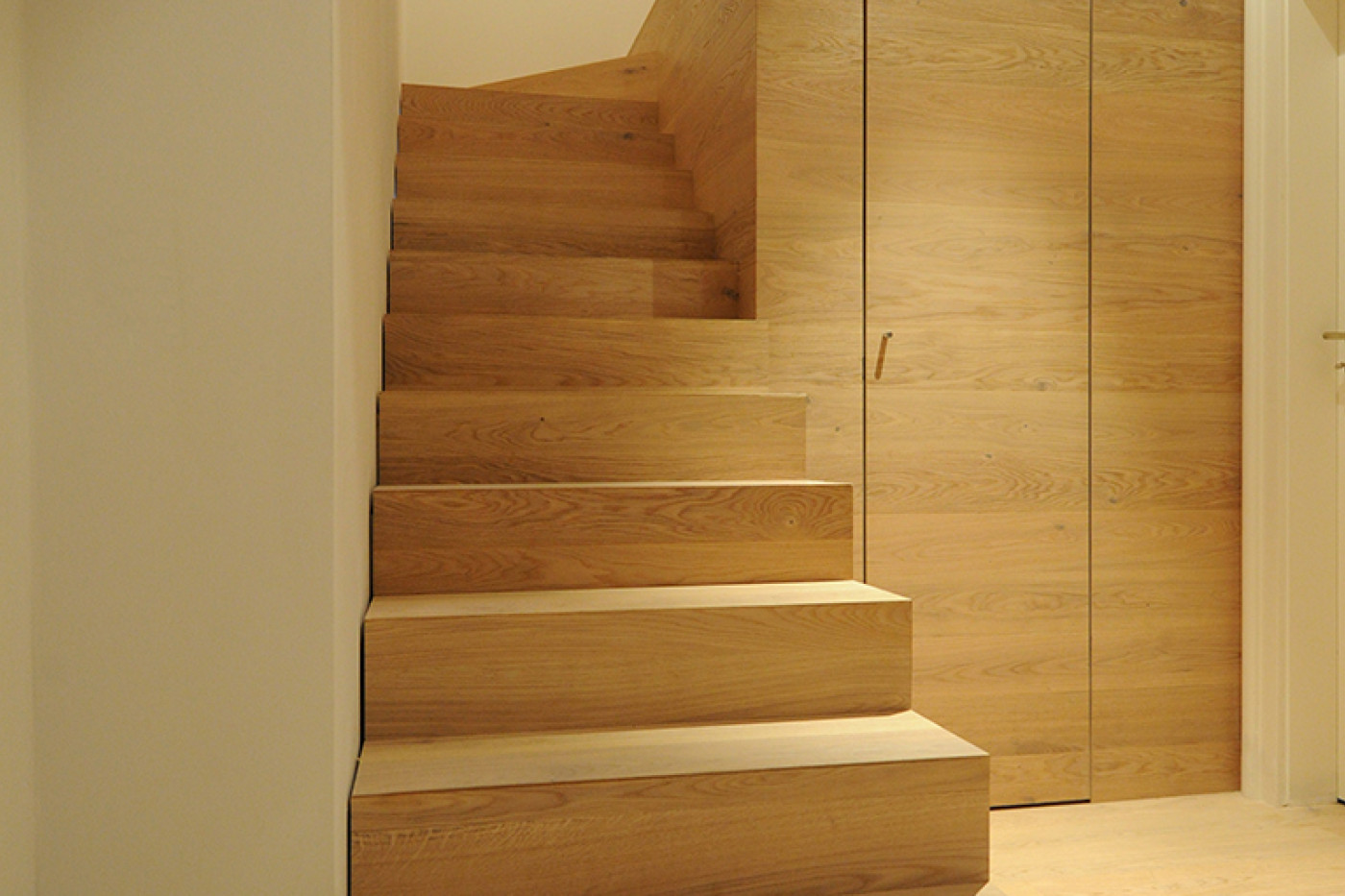 Neue Treppe aus Eiche mit massiven Stufen vor holzverkleideter Wand mit fl&auml;chenb&uuml;ndiger T&uuml;r.