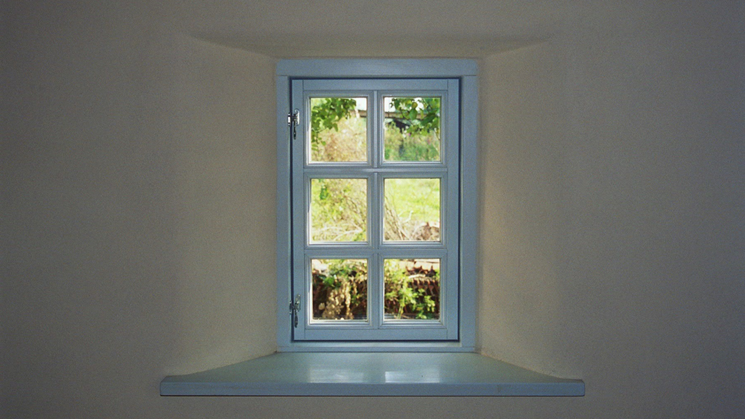 Tiefe wei&szlig;e Fensterlaibung mit hellblau gefasstem Sprossenfenster und Blick in den Garten.