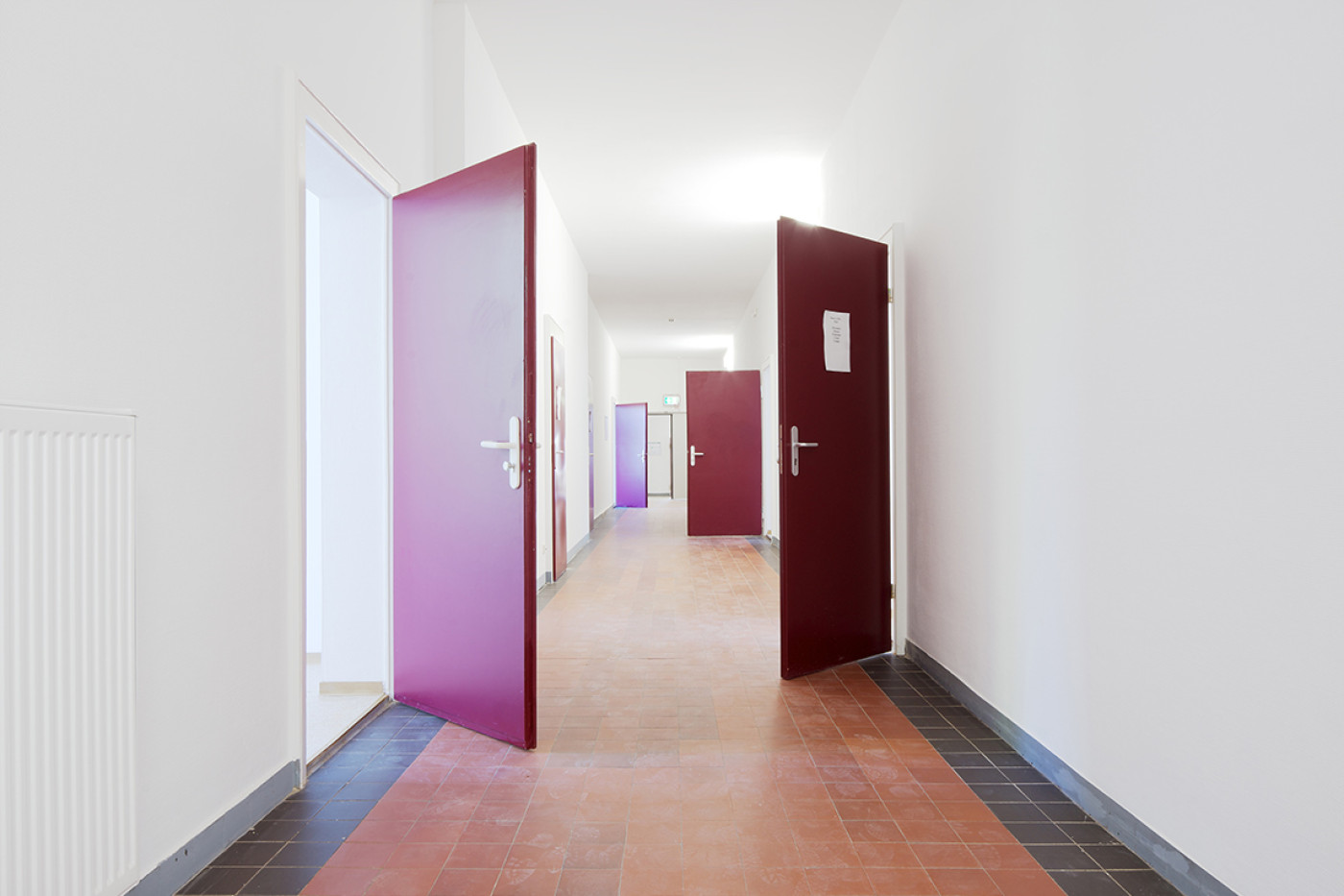 Corridor with a red-brown tiled floor and room doors standing open in magenta and claret.