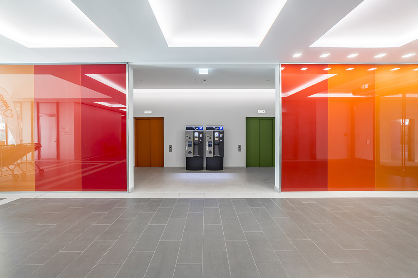 Passage mit rot und orange hinterlegten Glasw&auml;nden, dahinter zwei T&uuml;ren in Braun und Gr&uuml;n sowie zwei Automaten.