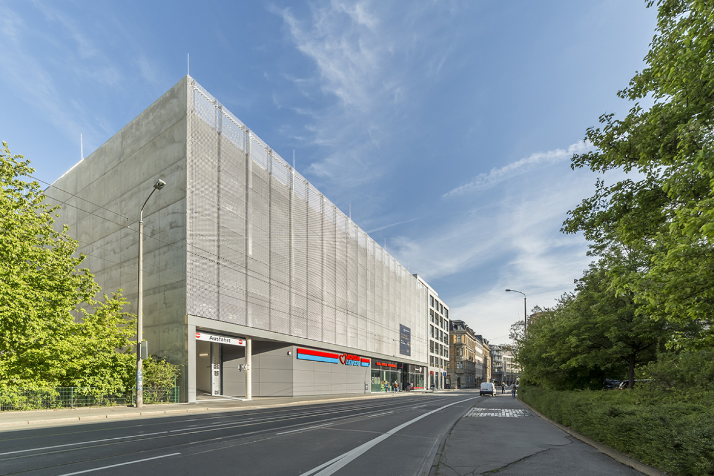 Parkhaus mit Sichtbetonfassade hinter einer Verkleidung aus Streckmetall, davor die Stra&szlig;e.