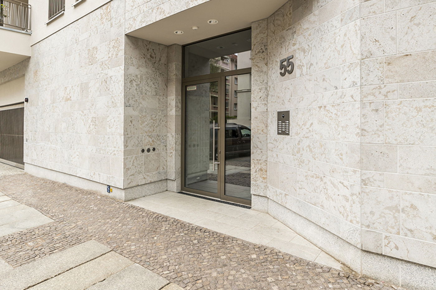 Entrance with natural stone cladding, the number 55 and a glazed door, a paved path in front.