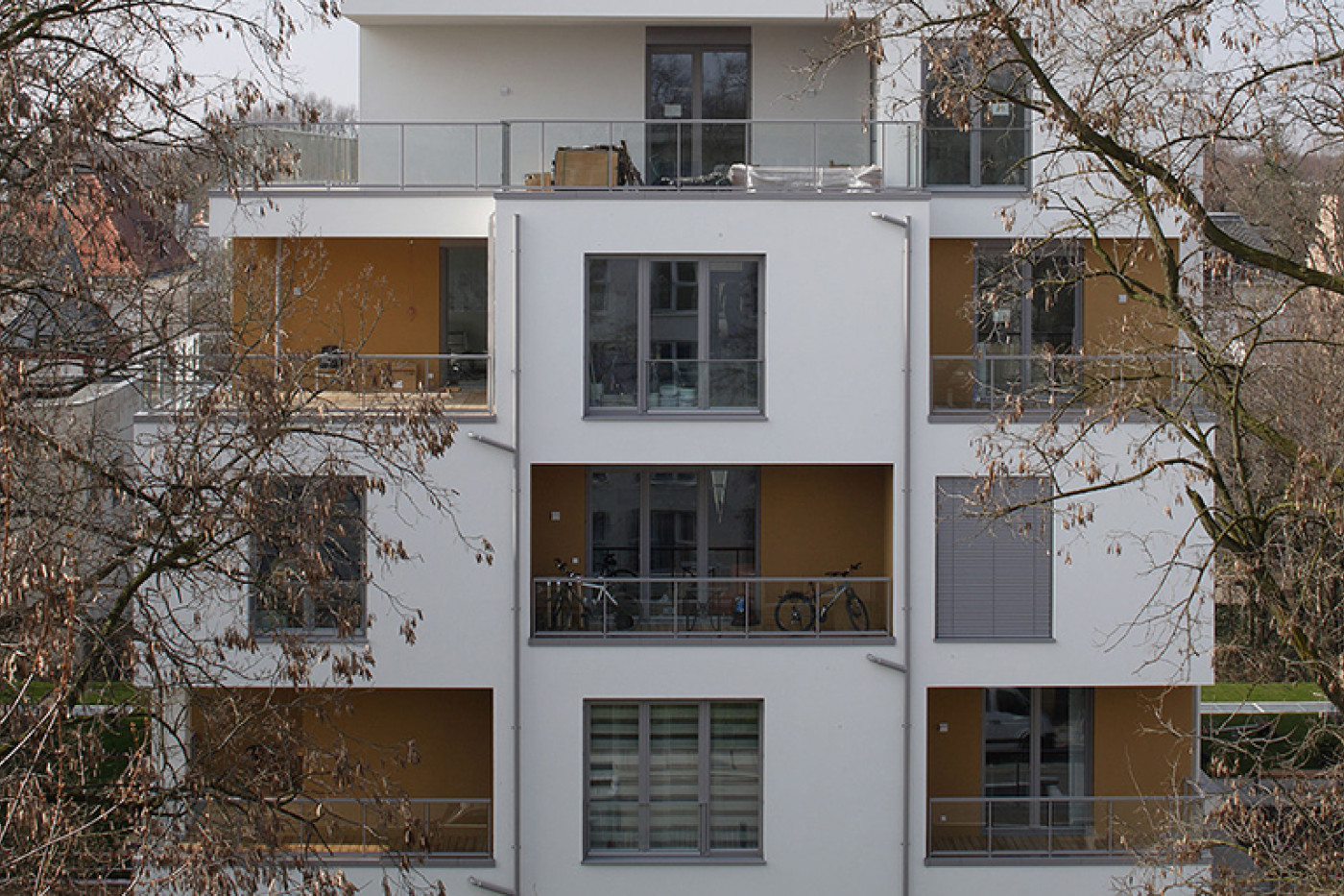 Gartenseite eines der Wohnh&auml;user mit ockerfarbenen Balkonnischen und Dachterrasse, gerahmt von kahlen &Auml;sten.