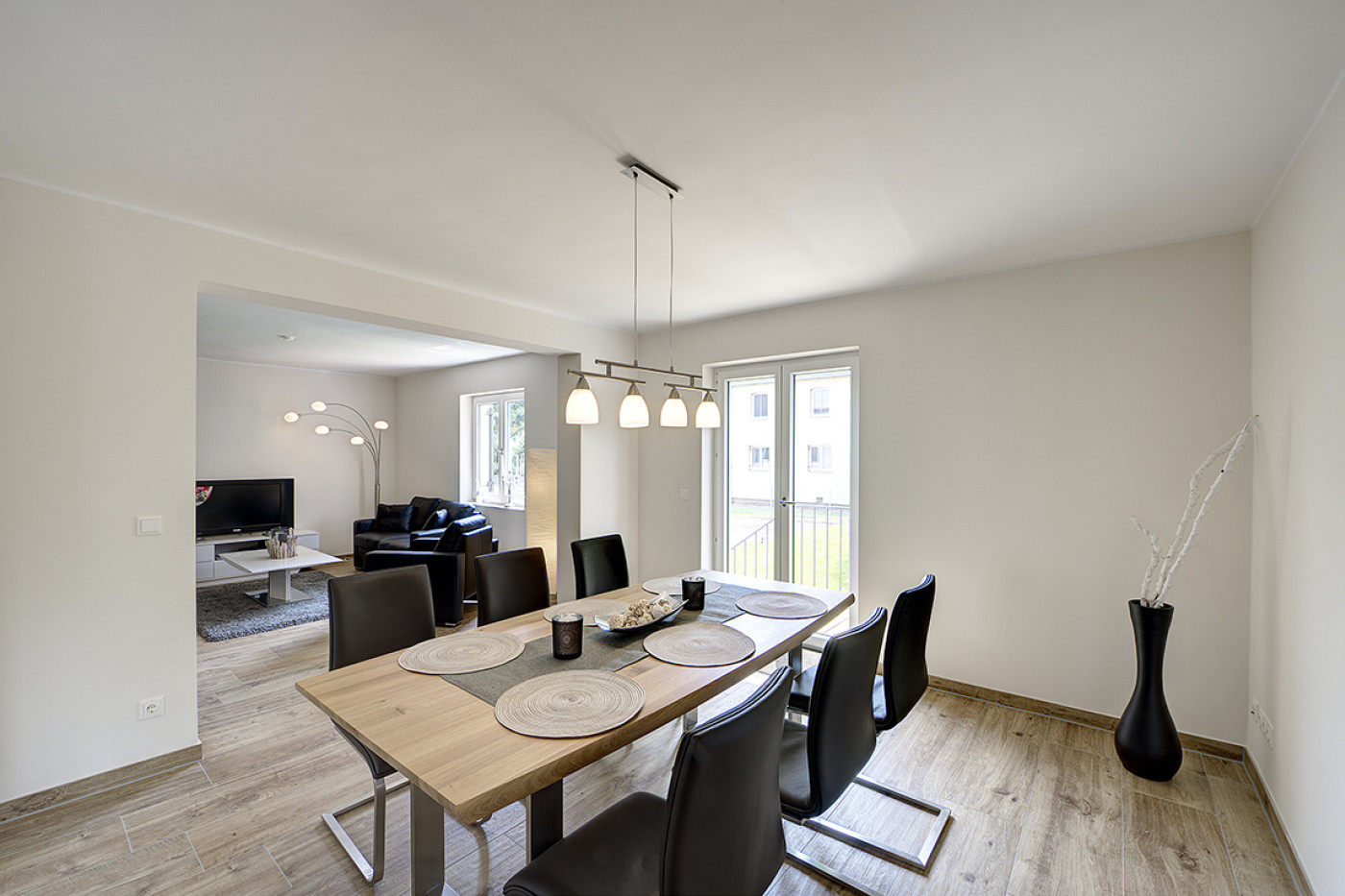 Essbereich mit Holztisch, dunklen St&uuml;hlen und Pendelleuchte, im Hintergrund der offene Wohnraum.